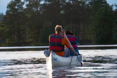 Zwei Personen paddeln in einem Kanu auf einem ruhigen See und tragen Schwimmwesten.