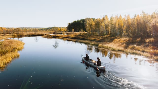 Ein Paar genießt die ruhige und unberührte Natur beim Kanufahren auf spiegelglattem Wasser.