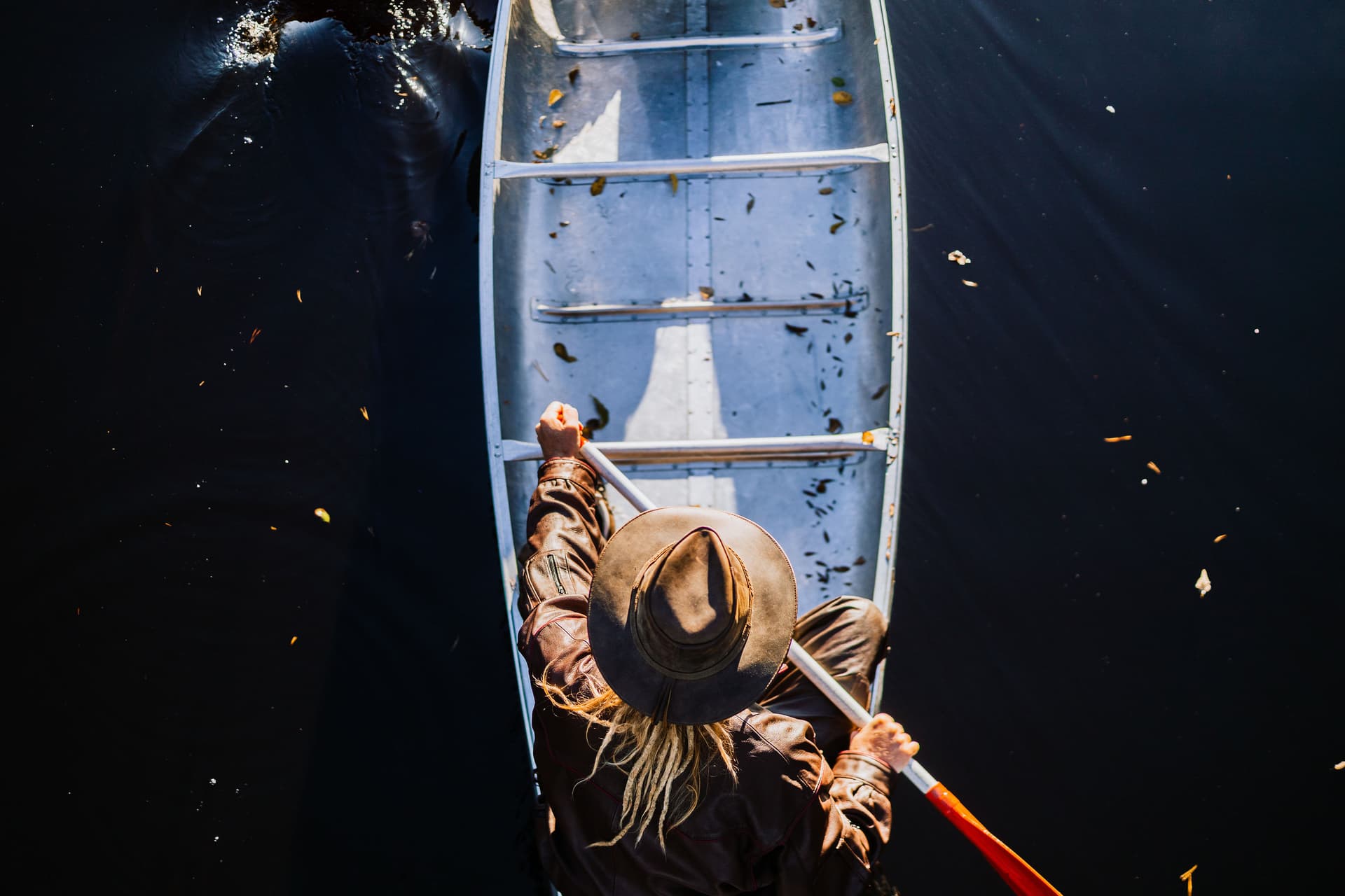 Een man in een cowboyhoed vaart in een kano op rustig water en geniet van de prachtige natuur.