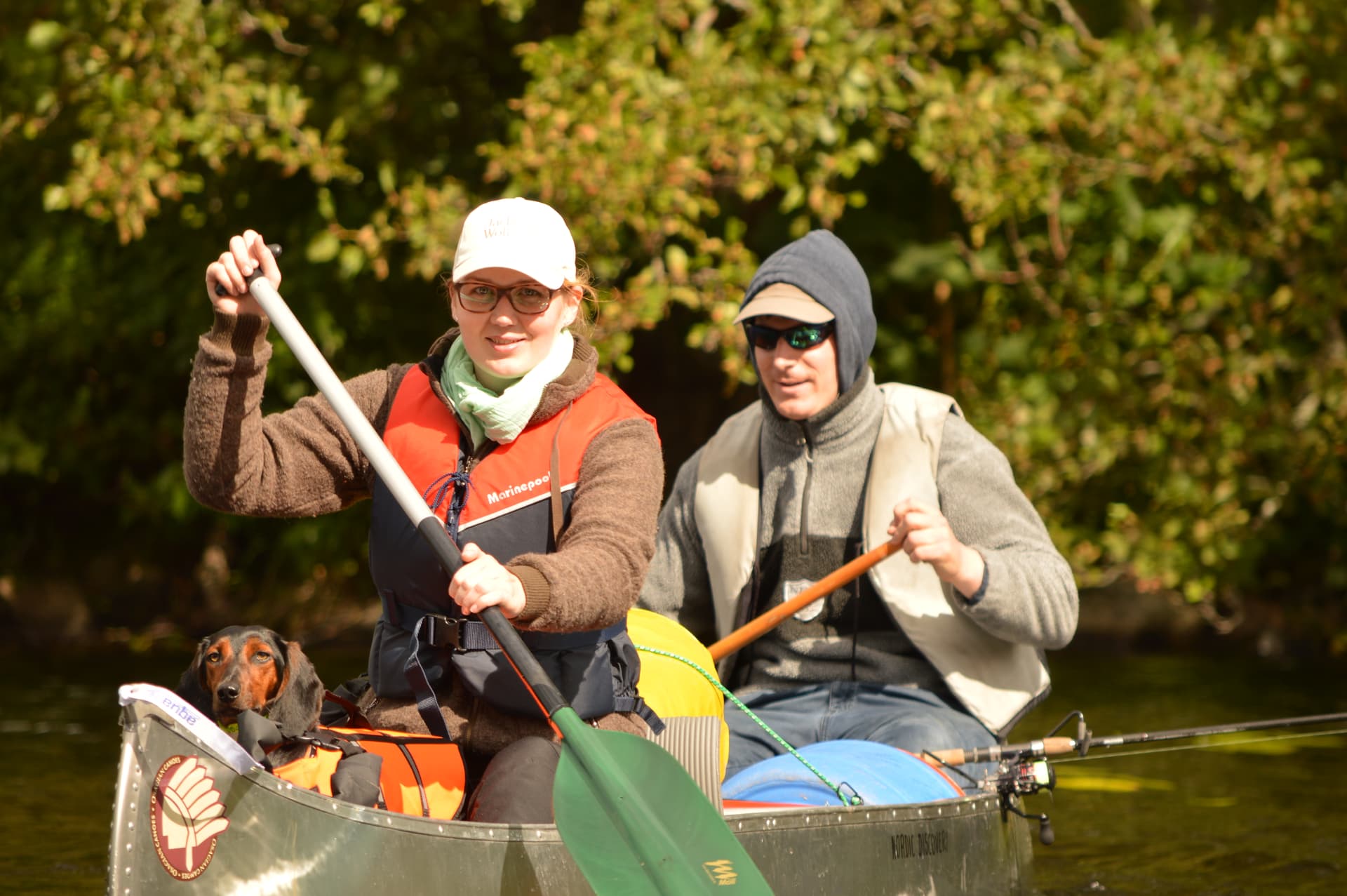 A fisherman with his wife and dog having a great time canoeing in the lush and green nature.