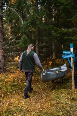 En man transporterar en kanot på hjul genom skogen till floden för en dag med paddling.