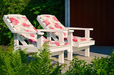 Deux chaises longues sur la véranda à l'extérieur du gîte en pleine nature sous le soleil estival suédois.
