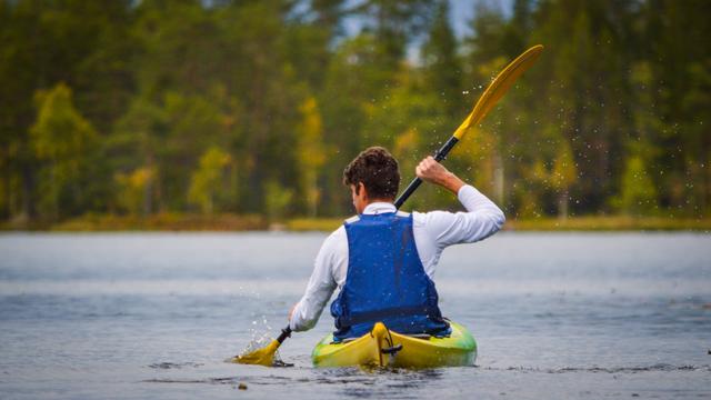 Un giovane in un viaggio in kayak che rema in modo che l'acqua schizzi dietro di lui.