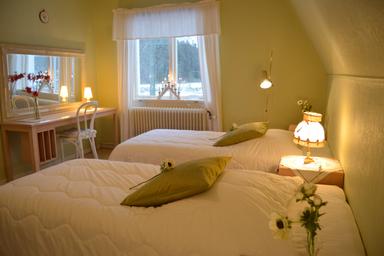 Gemütliche Atmosphäre mit frisch bezogenen Betten und Blumen im Elchzimmer in der wilderness lodge in Schweden.