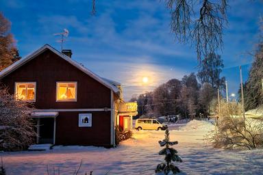 Wilderness Lodge i Sverige på natten med lamporna på. Månen lyser på himlen.