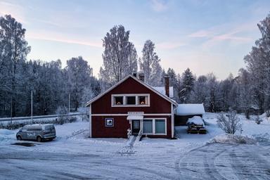 Den traditionella svenska Wilderness Lodge med en röd och vit träfasad i vinterlandskapet. Himmelen är blå med tunna moln.