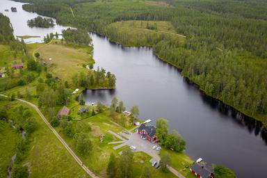 A bird's eye view of the river lodge in the middle of the Swedish wilderness with the lake in the background surrounded by deep forests.