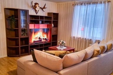 Vardagsrummet på River Lodge med en TV, en soffa och utsikt över sjön och skogen.