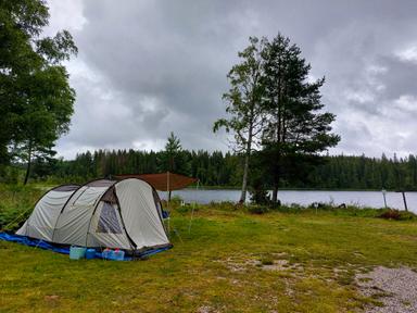 Ett tält är uppsatt på campingområdet vid vildmarkscamping med Sjön Söndagssjön i bakgrunden.
