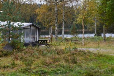 Ein Wohnwagen und eine Bank auf dem Wildnis-Campingplatz neben dem Wasser.