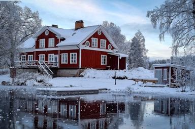Il rifugio sul fiume si trova in mezzo a un paesaggio invernale innevato con ghiaccio sul lago e neve sugli alberi.