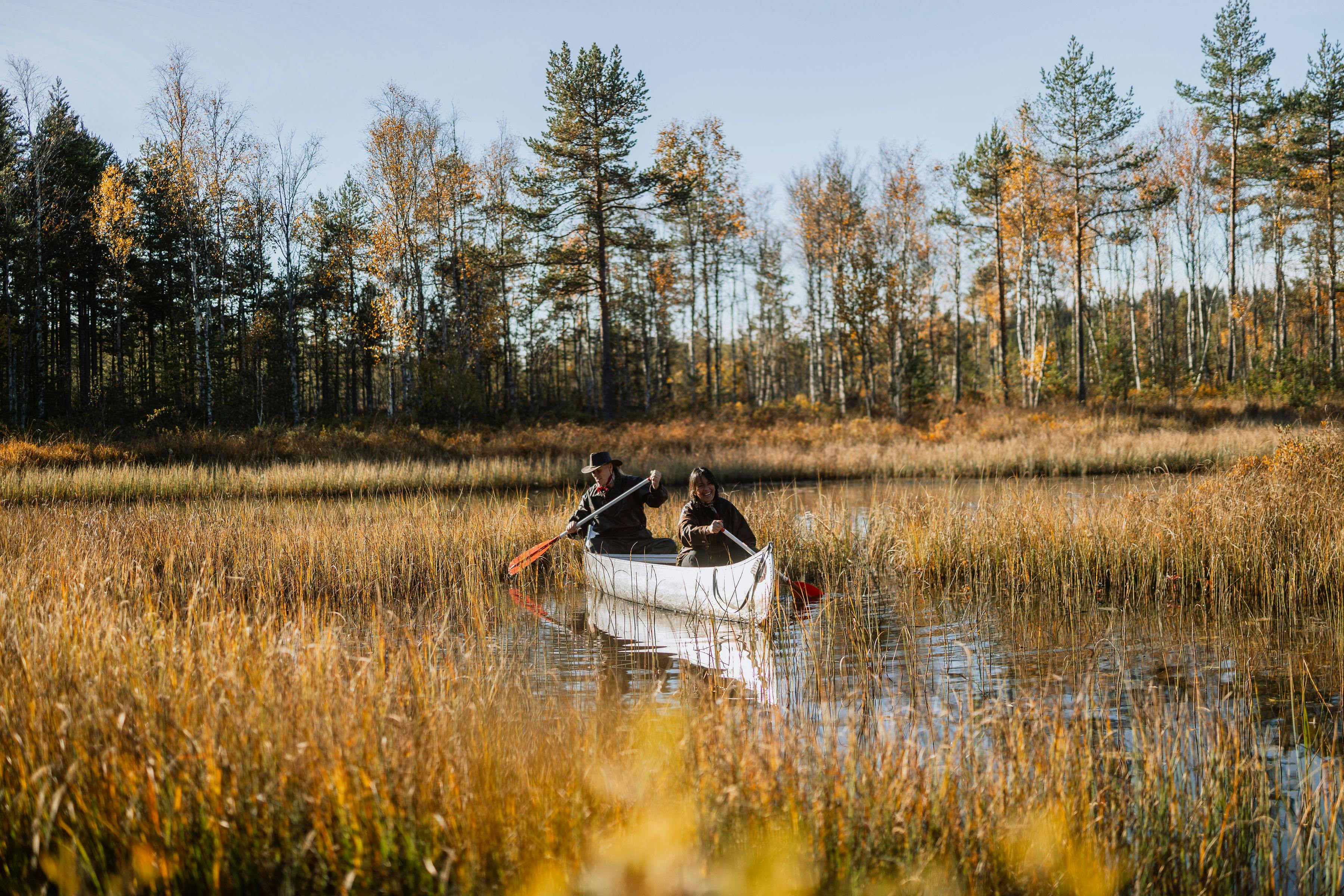 Två glada äventyrare utforskar den svenska vildmarken med kanot på en lugn flod.