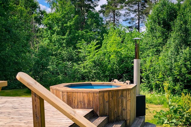 Wood-heated hot tub in the sunshine surrounded by green trees.