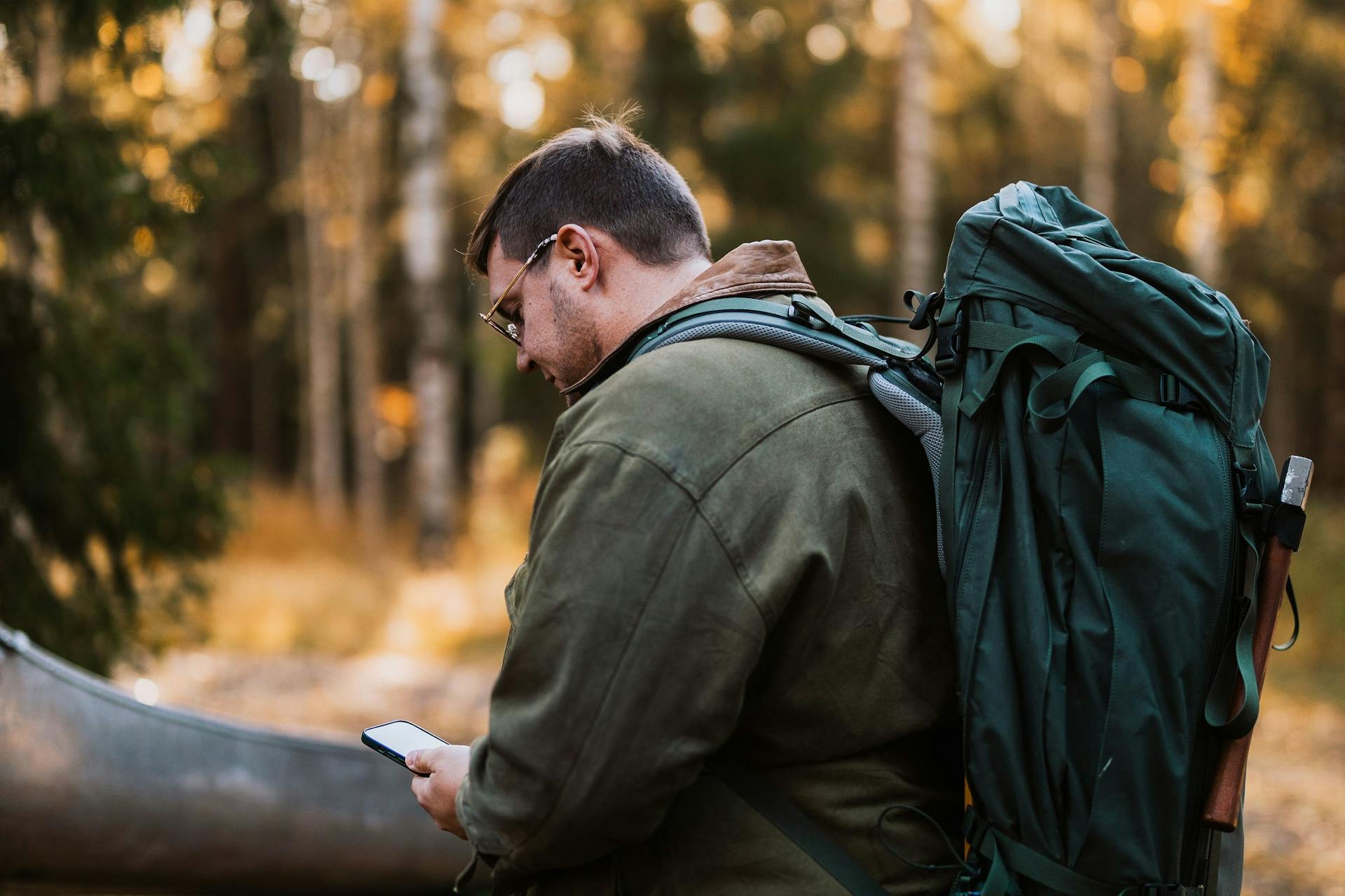 Vandrare med ryggsäck tittar på karta på sin telefon för att hitta rätt väg i den svenska vildmarken.
