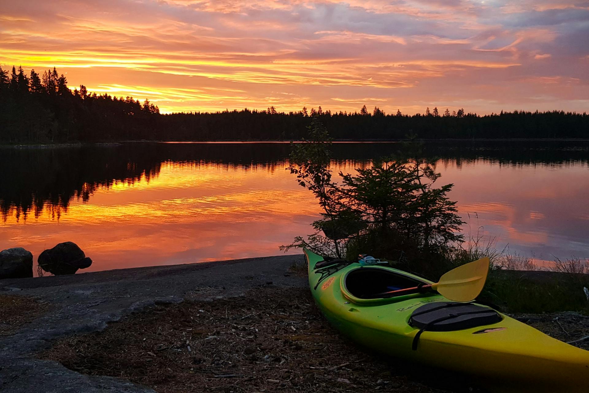 Kajak ligger på stranden av en sjö under en vacker solnedgång i naturreservatet Malingsbo-Kloten i Sverige.
