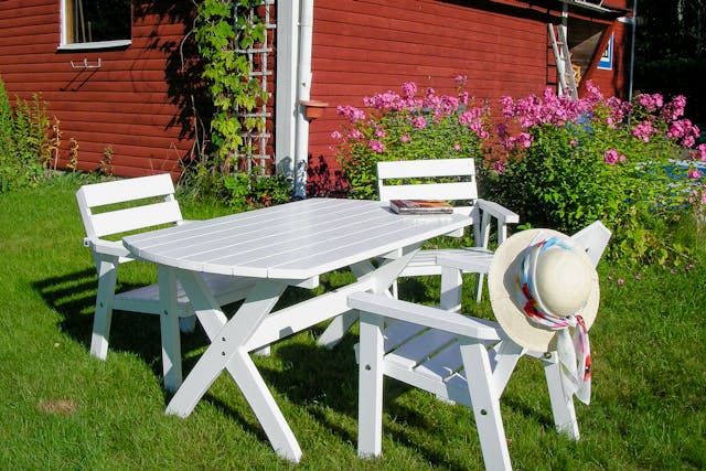 Tre sedie da giardino in legno bianco nel giardino del rifugio nella natura in Svezia. Un libro e un cappello da sole su una delle sedie.