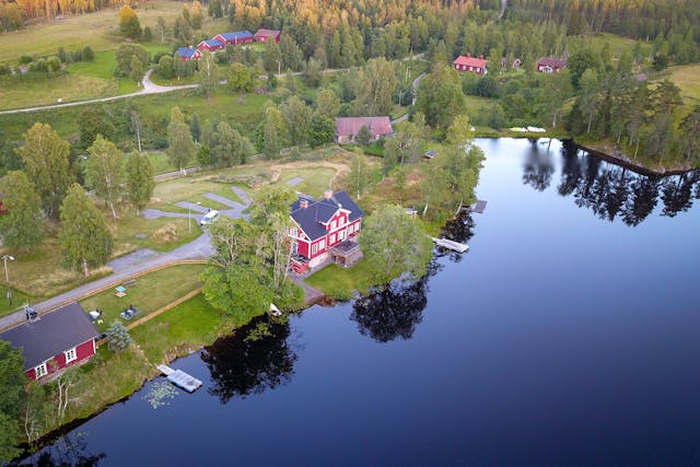 Una visión general de la propiedad de la cabaña del río y la zona de camping. El lago, el césped verde para montar tiendas de campaña y la sauna son visibles desde arriba.