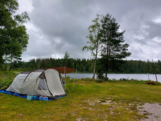 Een tent is opgezet op het campingterrein bij de wilderniscamping met het meer Söndagssjön op de achtergrond.
